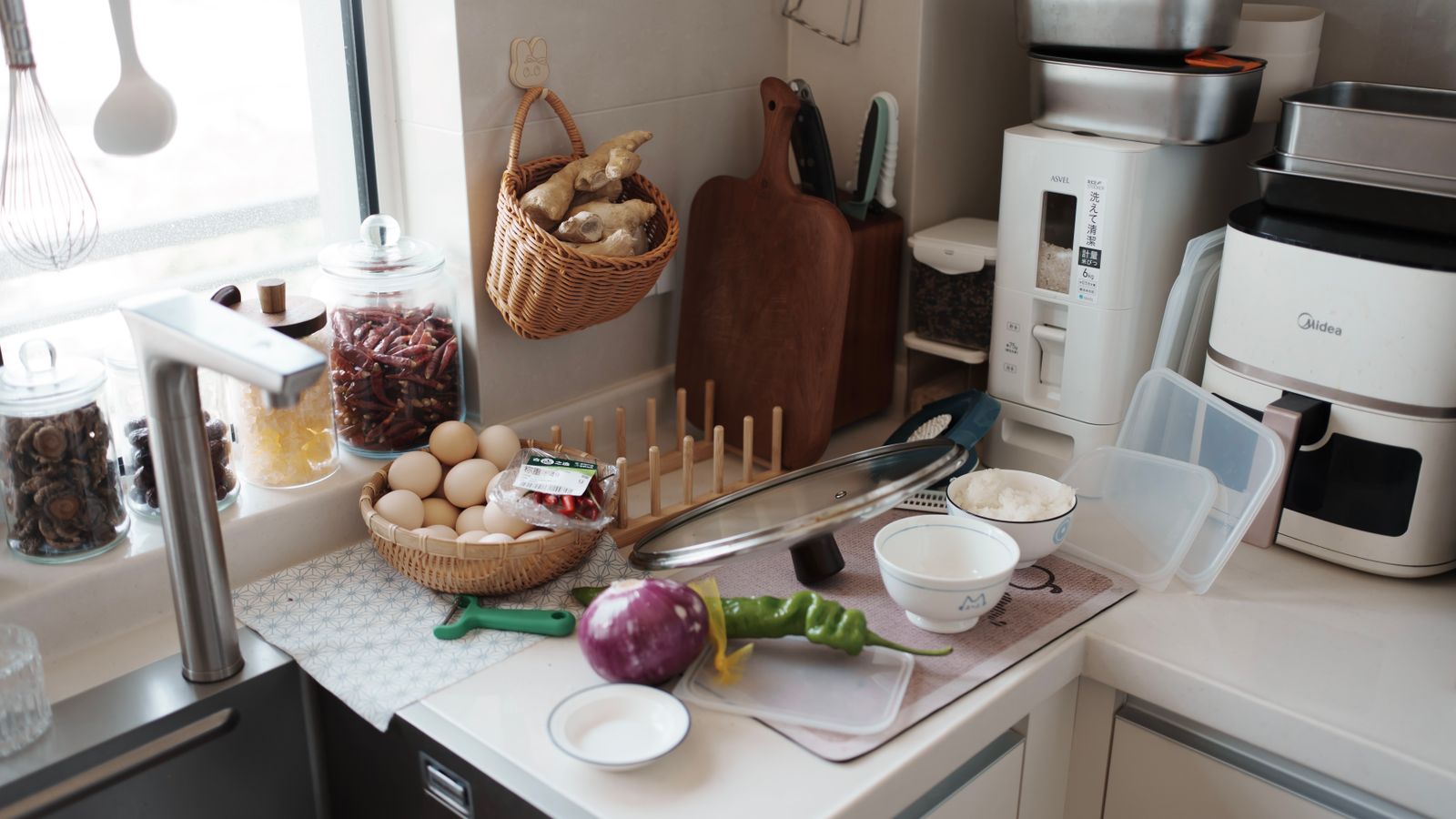 A kitchen counter with fresh ingredients ready for cooking, featuring eggs, vegetables, and kitchen gadgets.