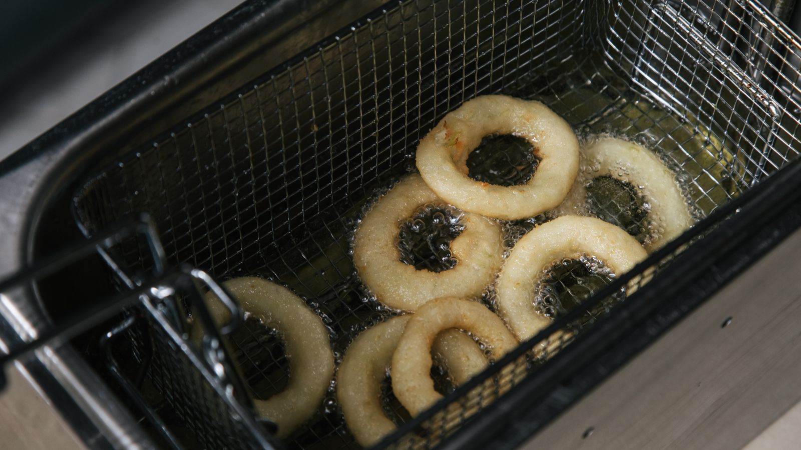 Hot crispy onion rings frying in oil in a deep fryer. Perfect food photography shot from above.