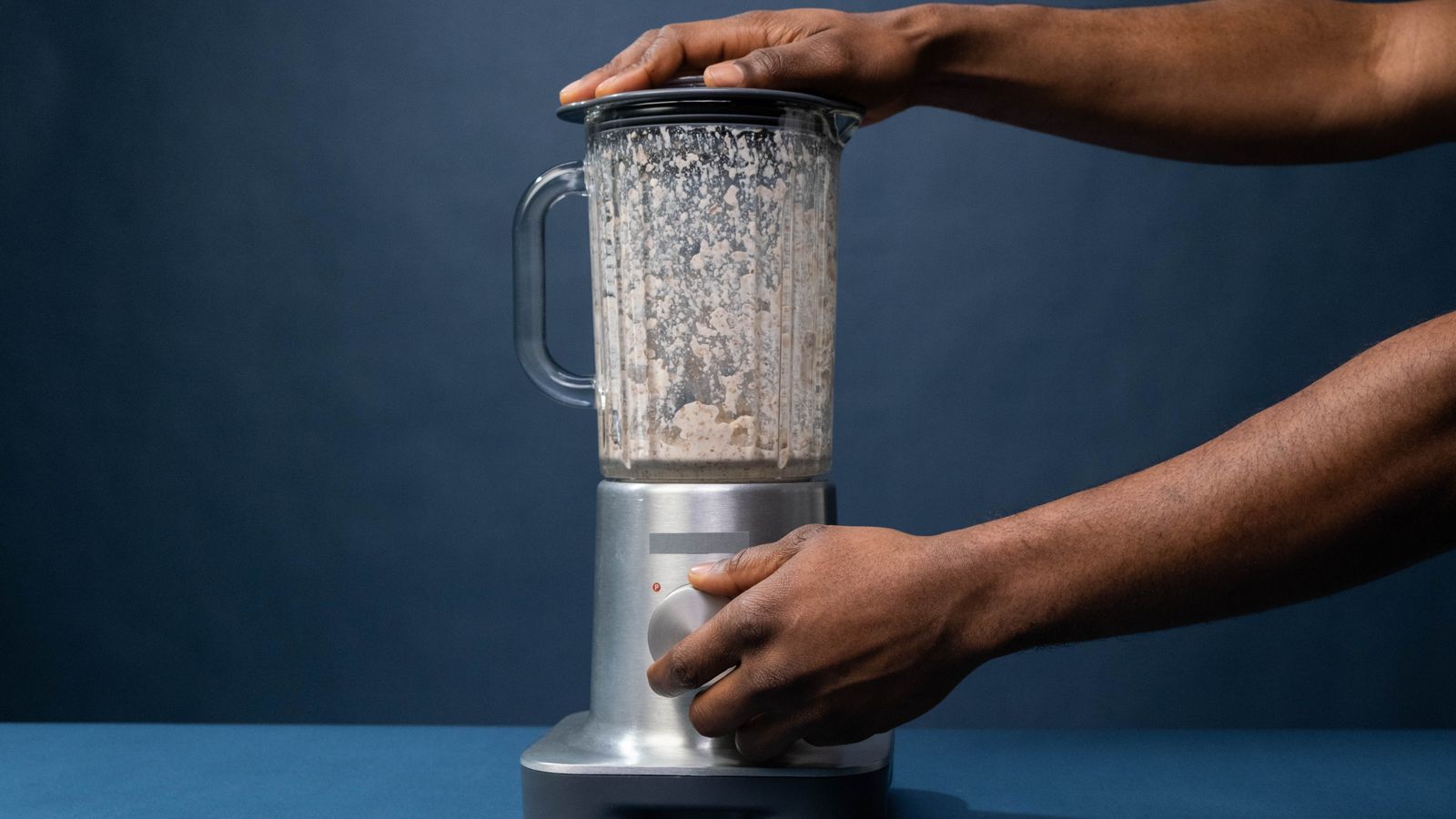 Close-up of male hands operating a blender in a kitchen setting.