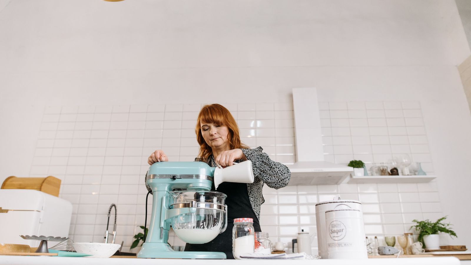 Woman pouring milk into a stand mixer while baking in a stylish kitchen.