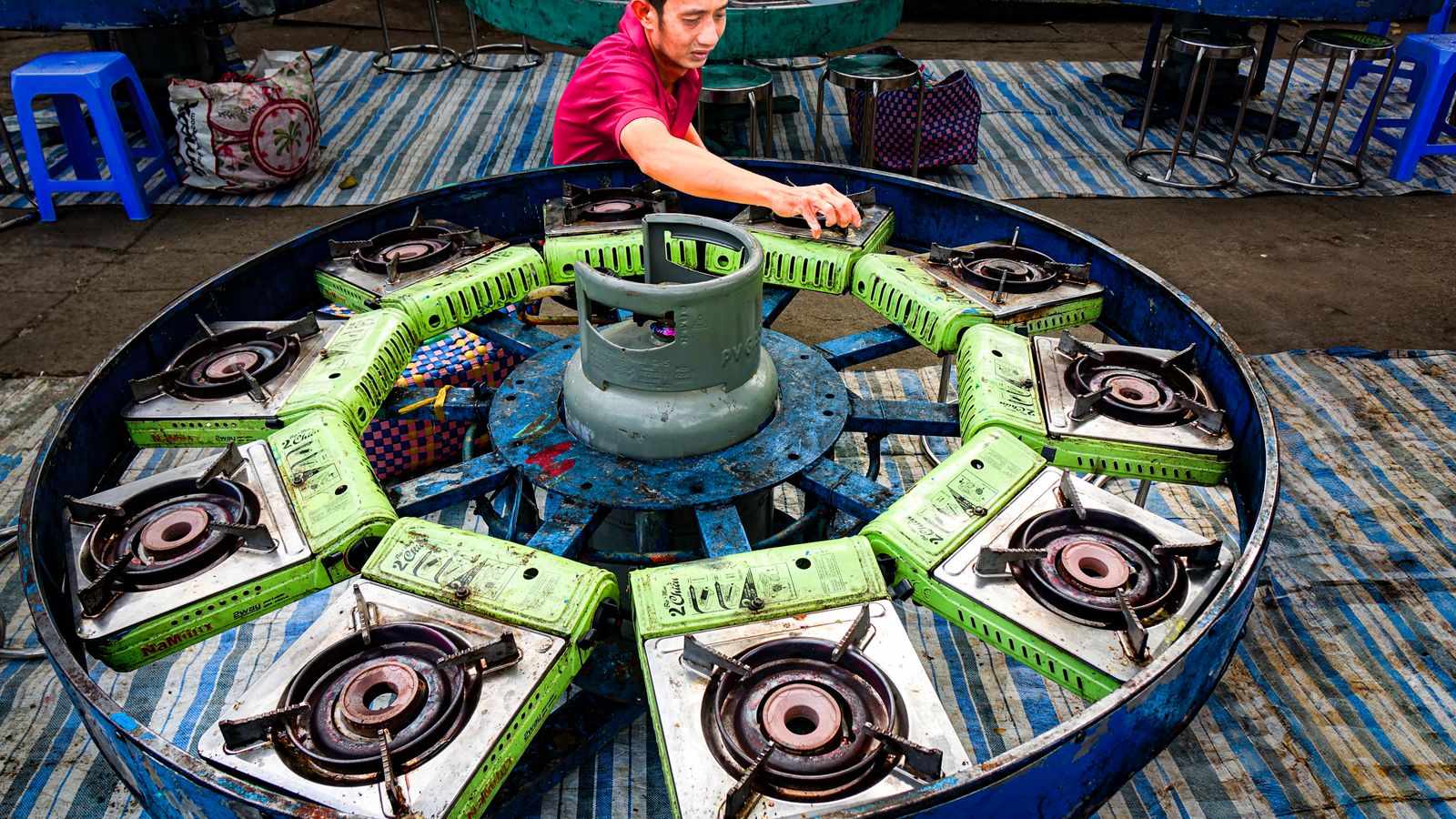 A man arranges stove burners around a central gas cylinder outdoors.