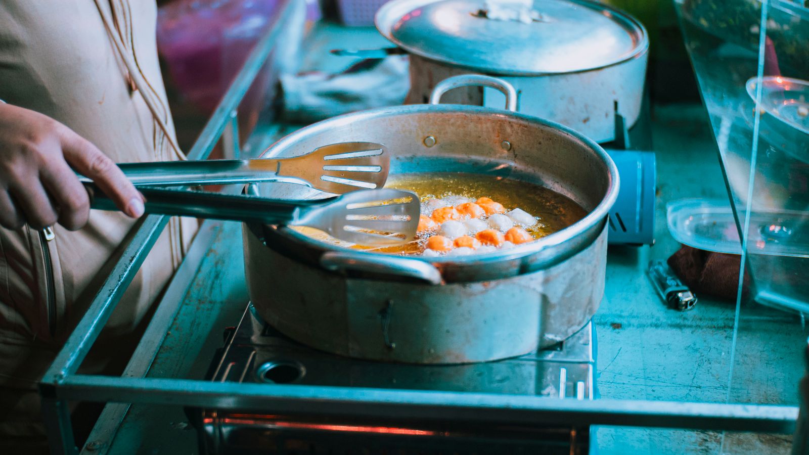 Close-up of a person frying food in a pan using tongs on a stove indoors.
