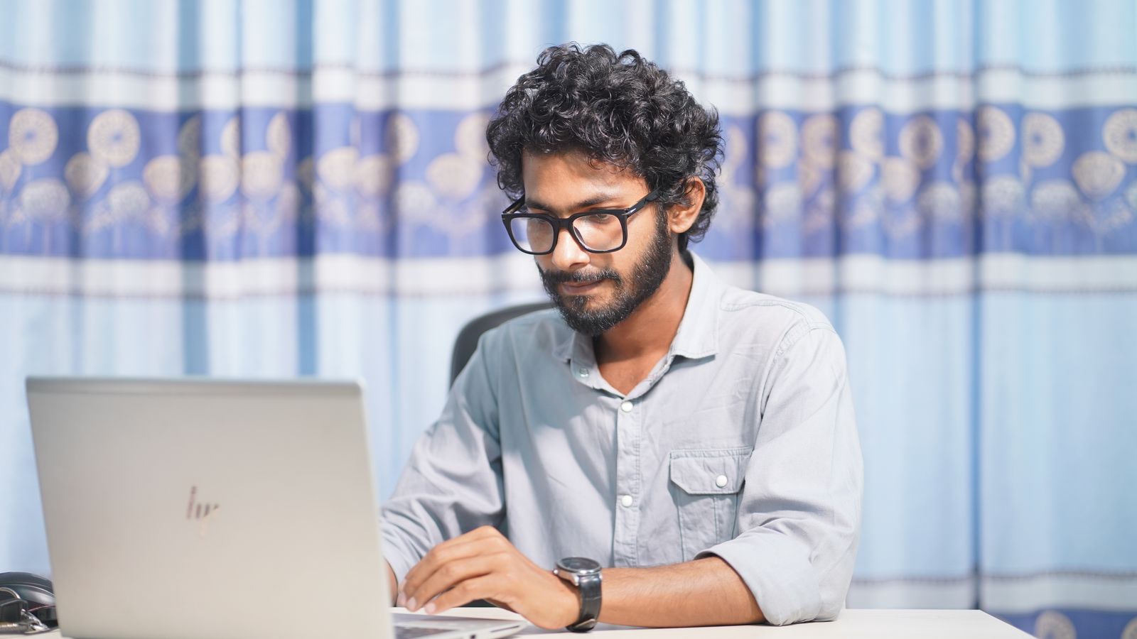 A focused young man using a laptop in a well-lit room. Ideal for themes of productivity and tech.