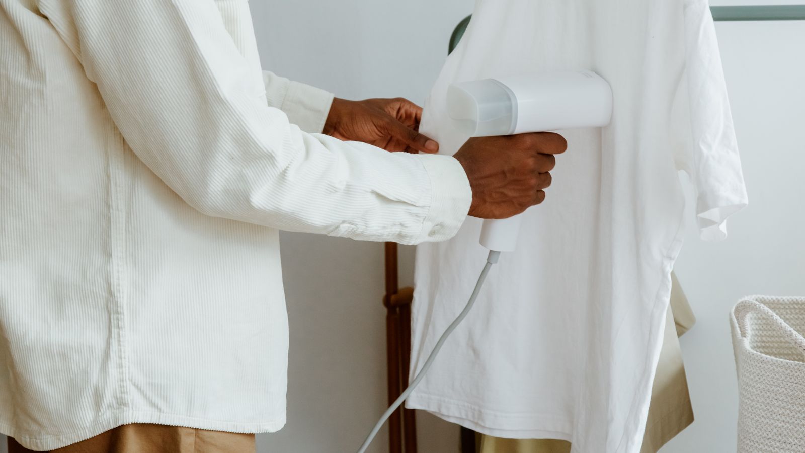 A man uses a steam iron to remove wrinkles from a white shirt hanging on a rack indoors.