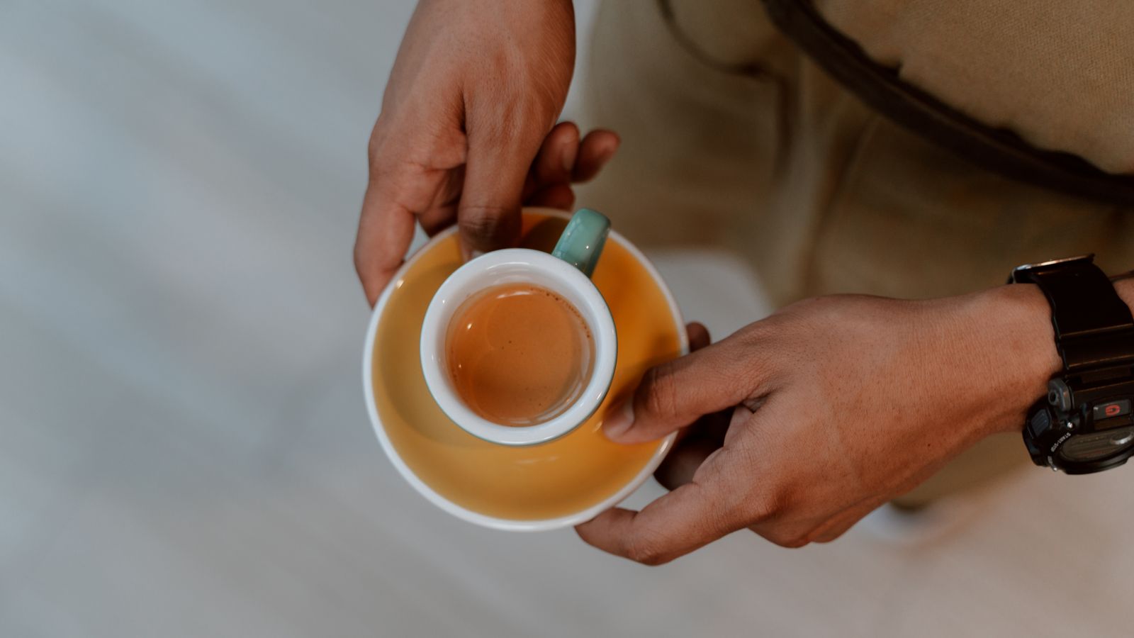A person holding a ceramic cup with freshly brewed espresso, photographed from above.