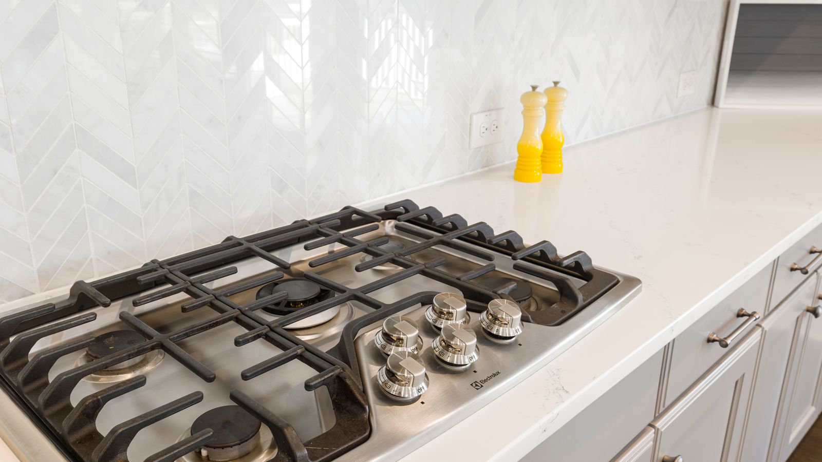 Sleek kitchen countertop featuring a gas stove and white tiled backsplash, with yellow salt and pepper shakers.