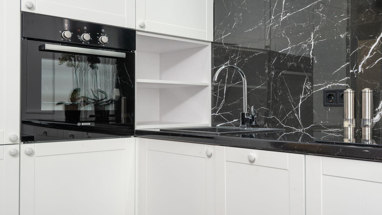 Interior details of modern kitchen with white cabinets and black glossy marble backsplash and modern appliances in daylight