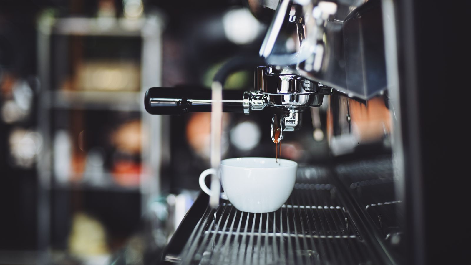 Close-up of espresso machine brewing coffee into a white cup in a cafe setting.