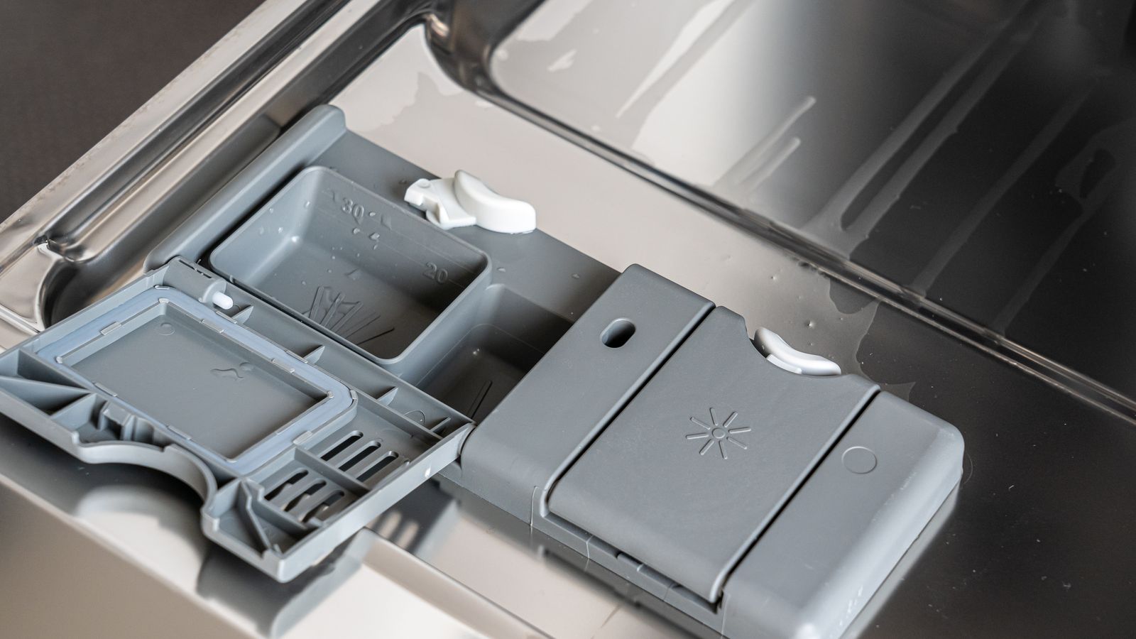 A detailed view of a dishwasher detergent compartment with soap residue.