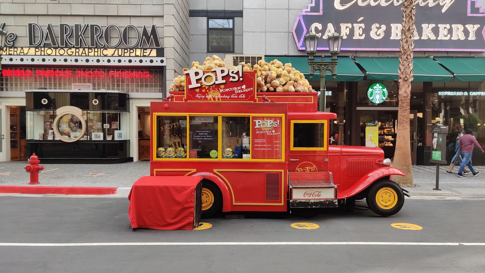Colorful vintage popcorn truck outside cafes and shops on a bustling street.