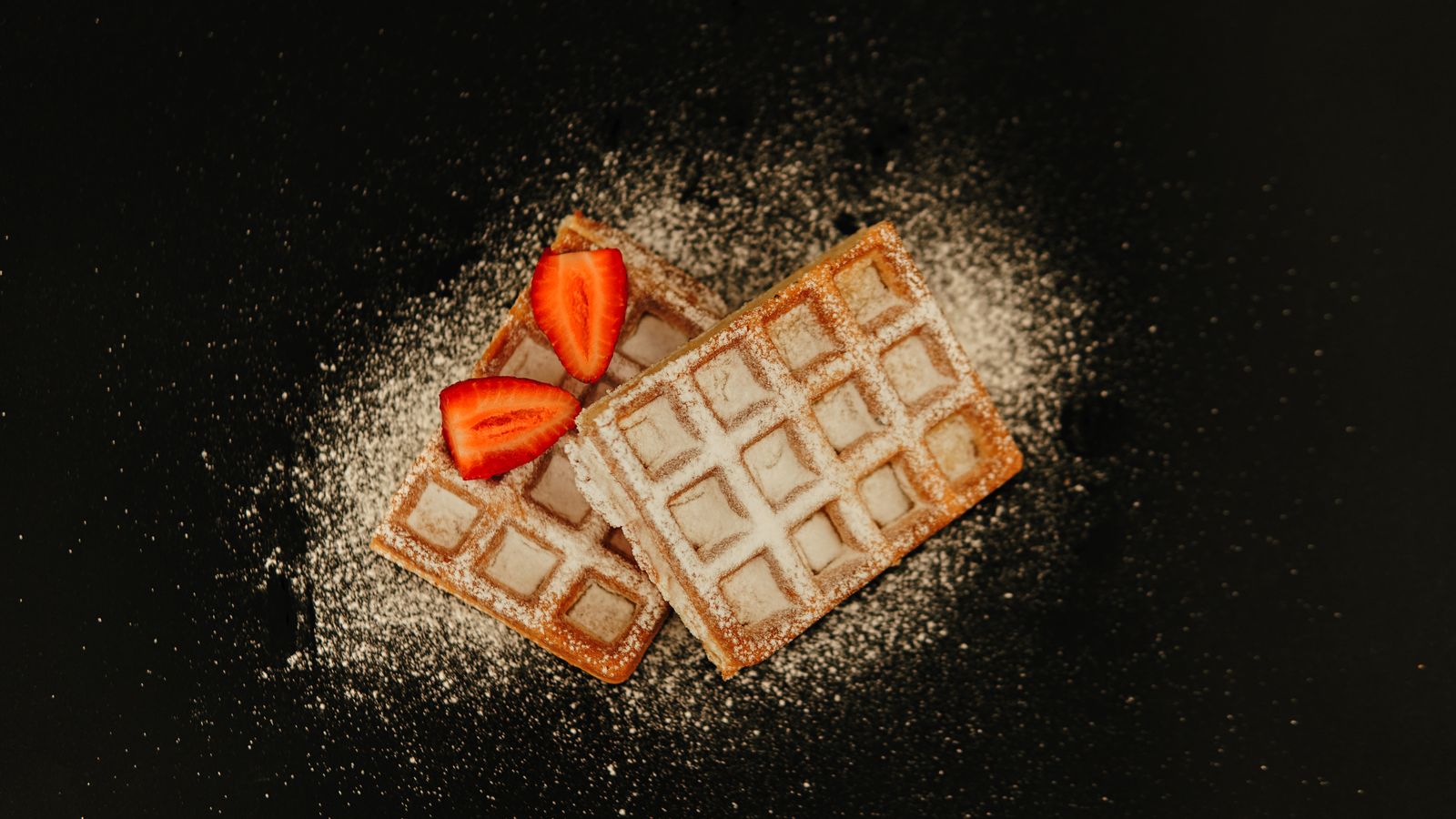 Tasty Belgian waffles topped with fresh strawberries and sugar dusting.