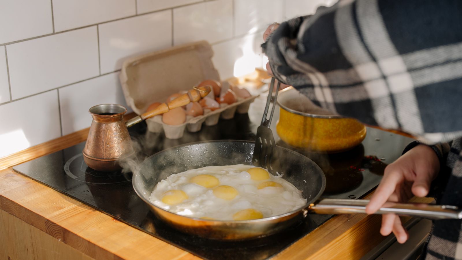Close-up of cooking eggs on a stovetop with human hands in a kitchen setting.
