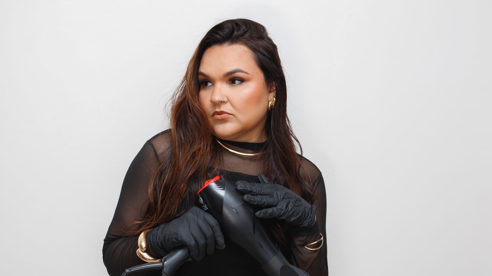Portrait of a woman in a salon holding a hair dryer, wearing elegant gloves and jewelry.