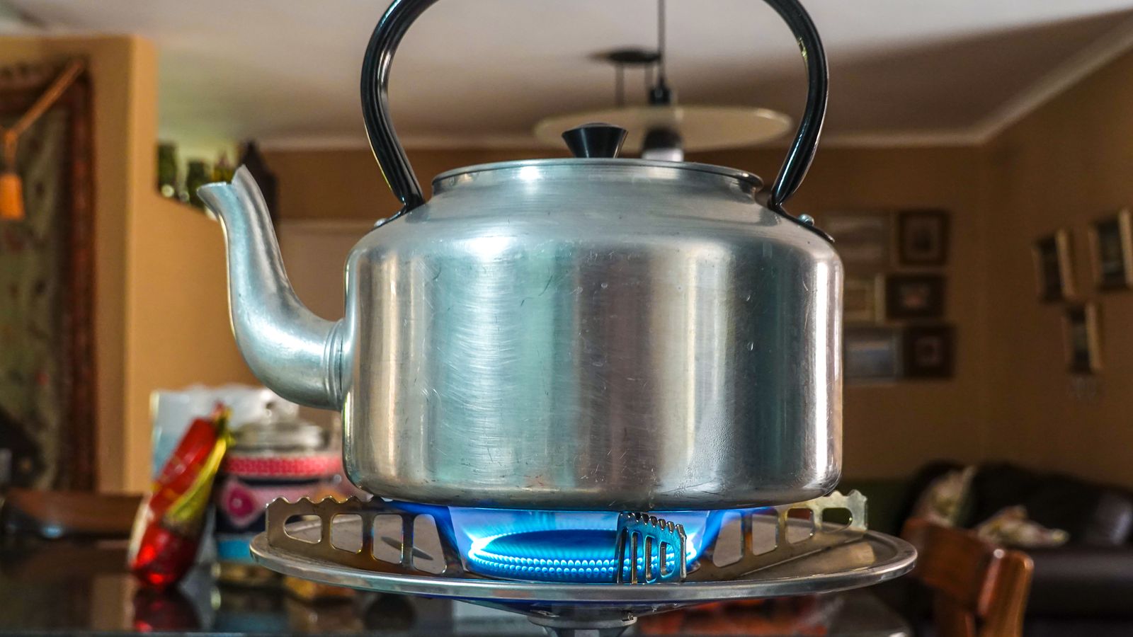 Close-up of a stainless steel kettle heating on a gas stove in a cozy kitchen setting.