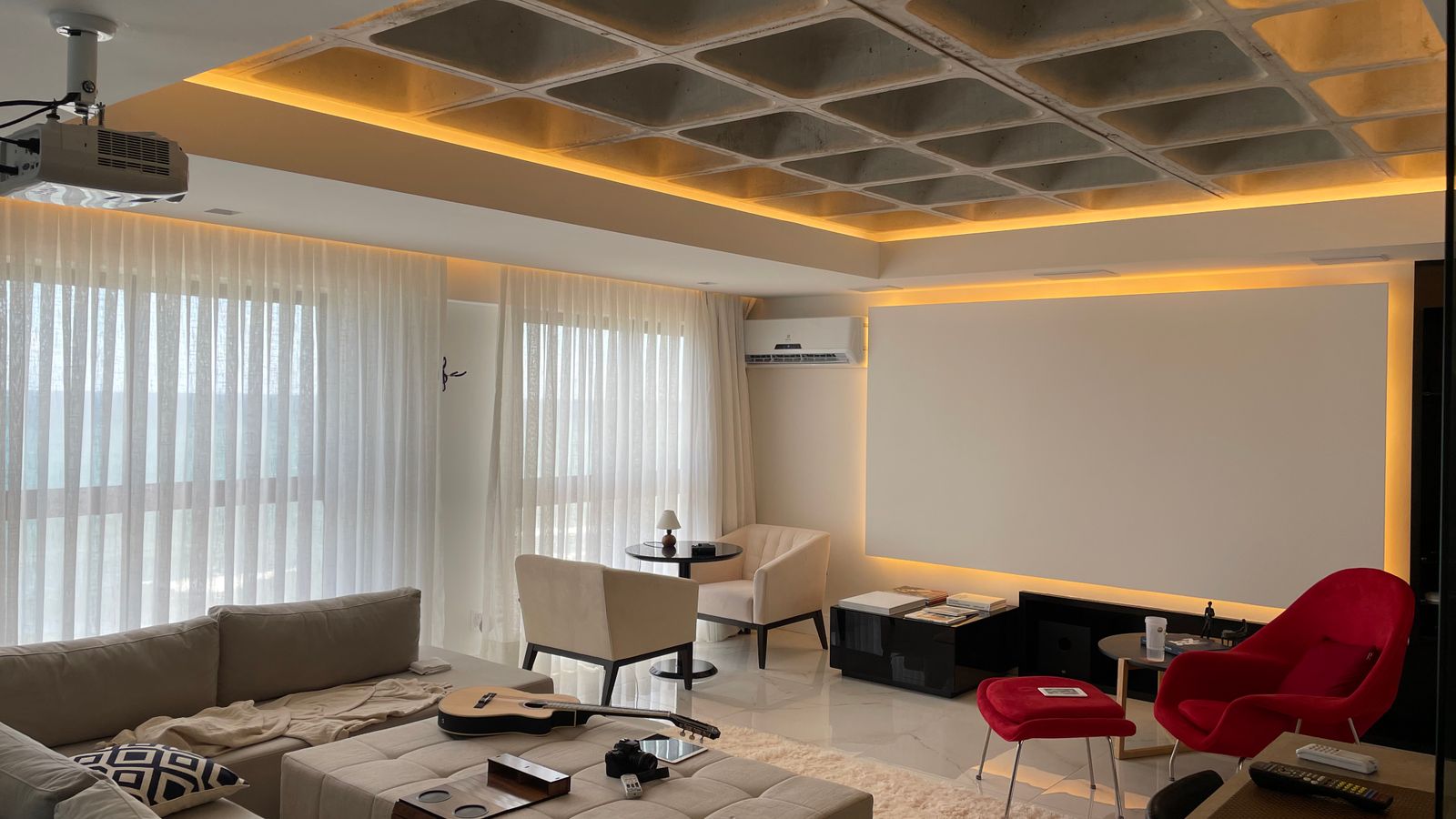 Spacious minimalist living room with natural light, featuring cozy seating and a ceiling projector.