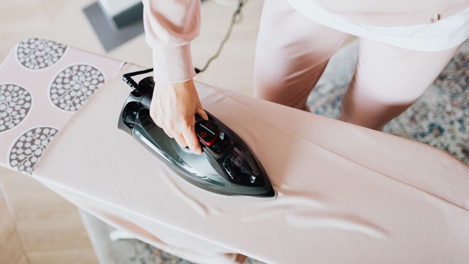 A person using a steam iron on a pink ironing board indoors, focusing on household chores.