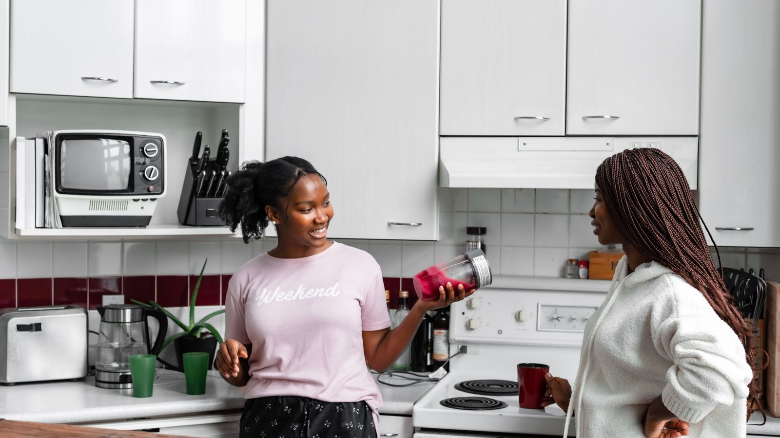 Two women in a modern kitchen making smoothies, enjoying casual conversation.