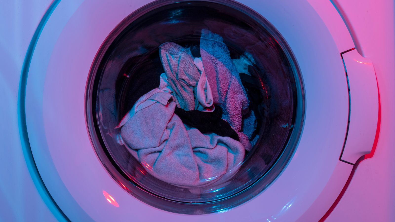 Colorful washing machine with clothes inside, lit by vivid purple and blue lights.