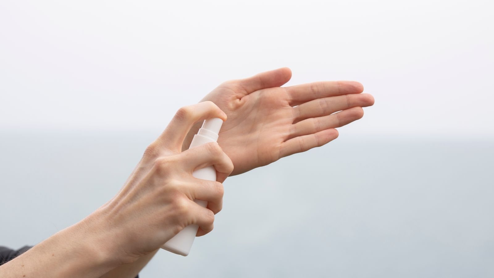 A person using hand sanitizer spray by the sea, promoting hygiene and cleanliness.
