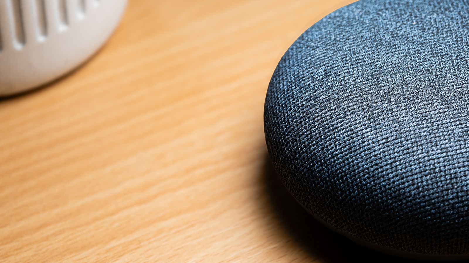 A close-up view of a smart speaker on a wooden table, capturing texture details.
