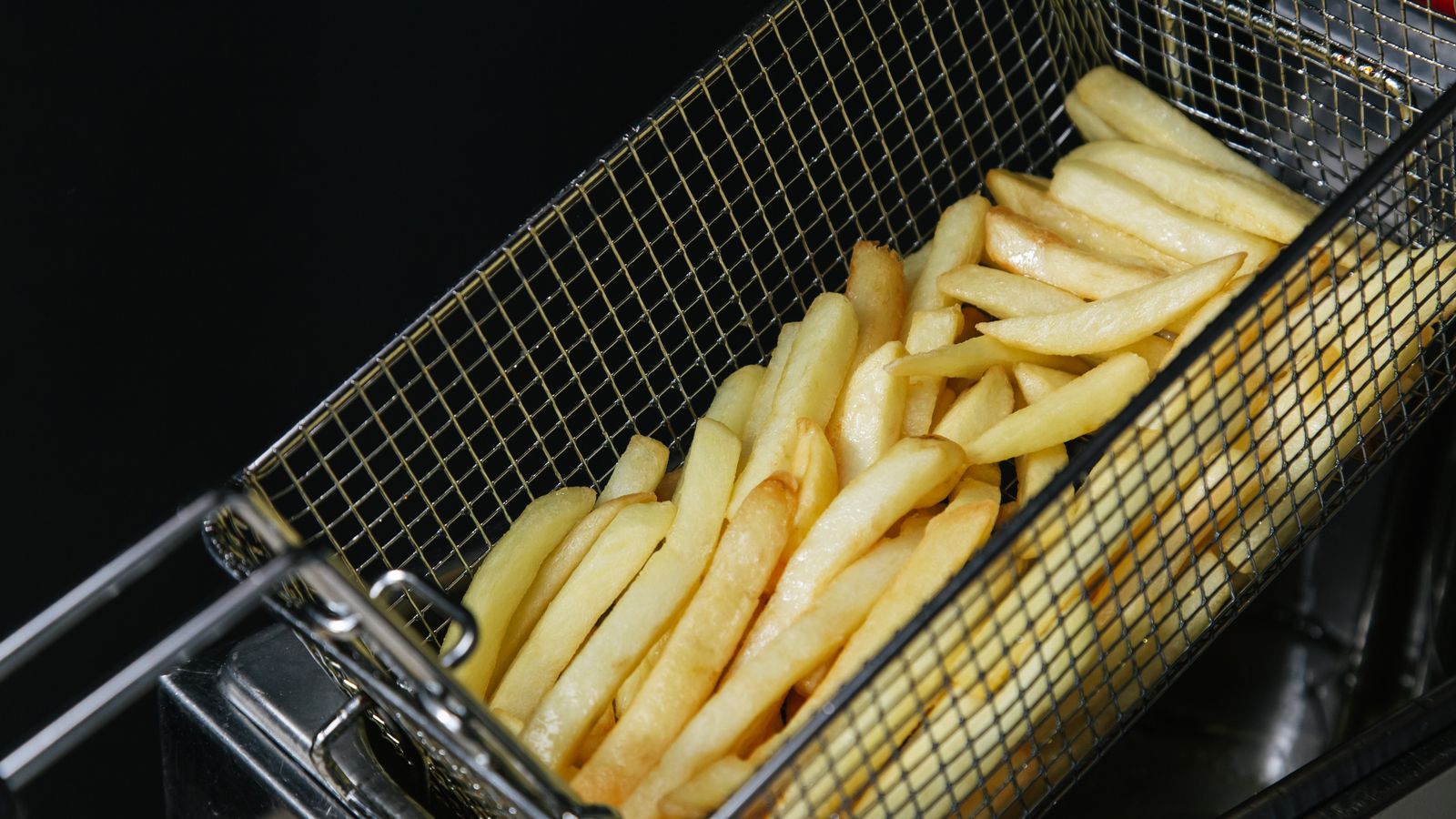 Close-up of freshly fried crispy French fries in a metal basket, highlighting fast food textures.