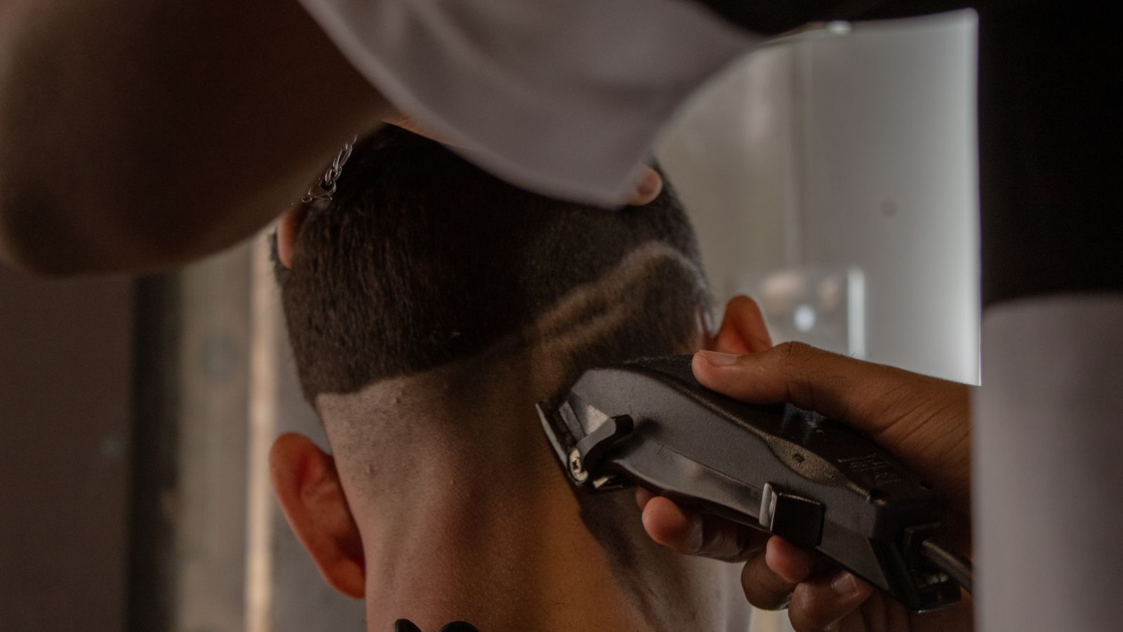 A detailed view of a barber using clippers to trim a man's hair indoors.