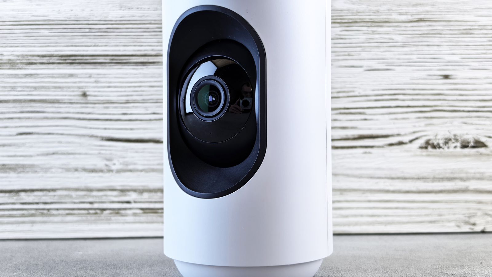 Stylish white home security camera placed on a wooden surface for indoor surveillance.