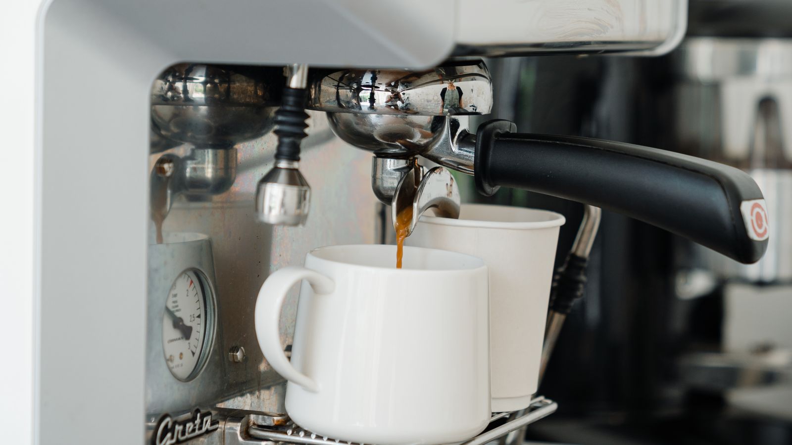 Coffee machine pouring fresh brewed aromatic coffee into ceramic mug and disposable cup