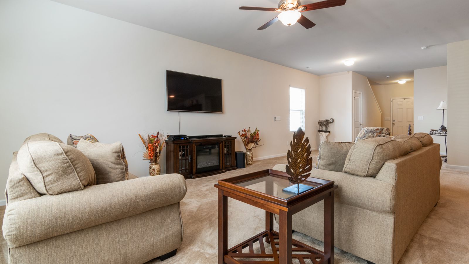 Spacious living room featuring neutral sofas, ceiling fan, and TV for a contemporary yet cozy feel.