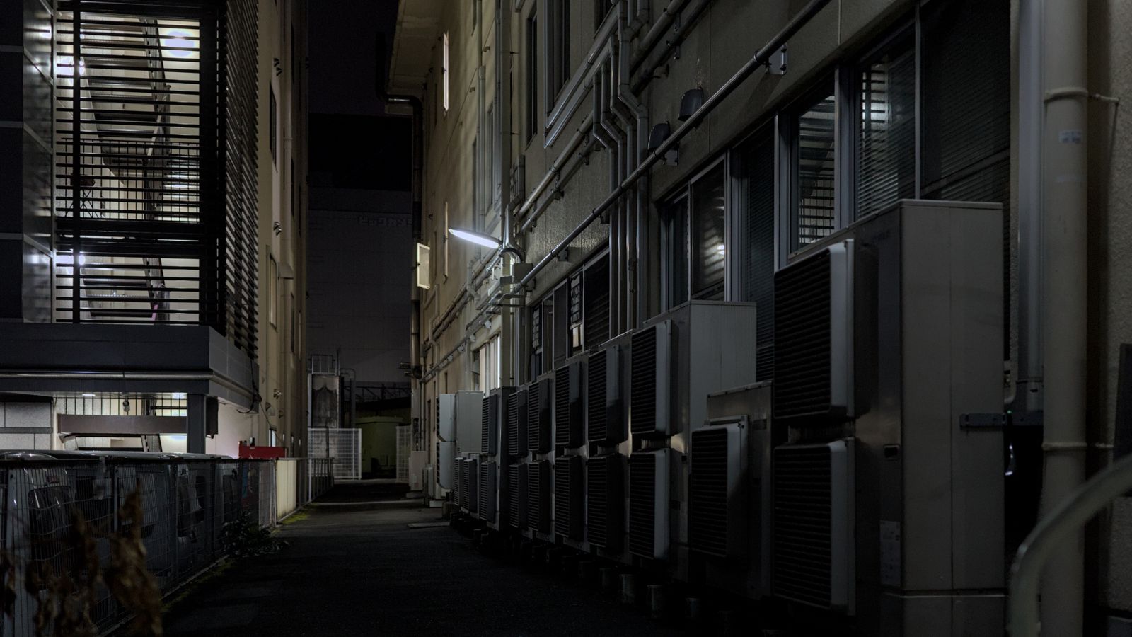 A dimly lit urban alley in Kyoto featuring air conditioning units, captured at night.
