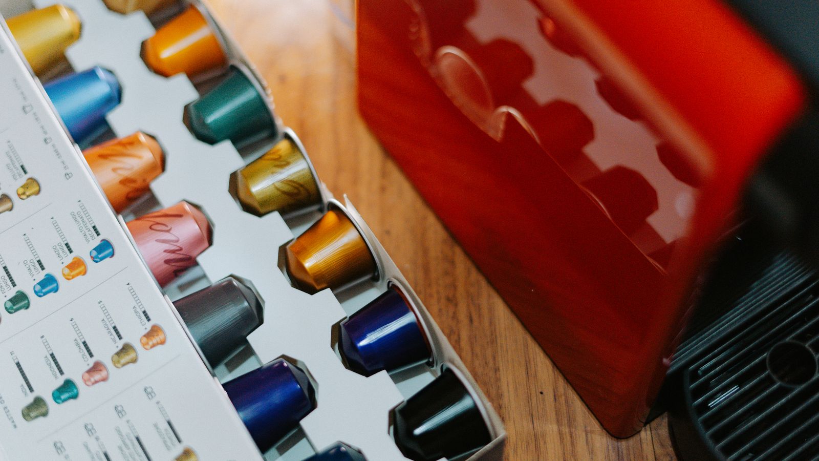 Close-up of colorful coffee capsules next to a coffee machine on a wooden table.