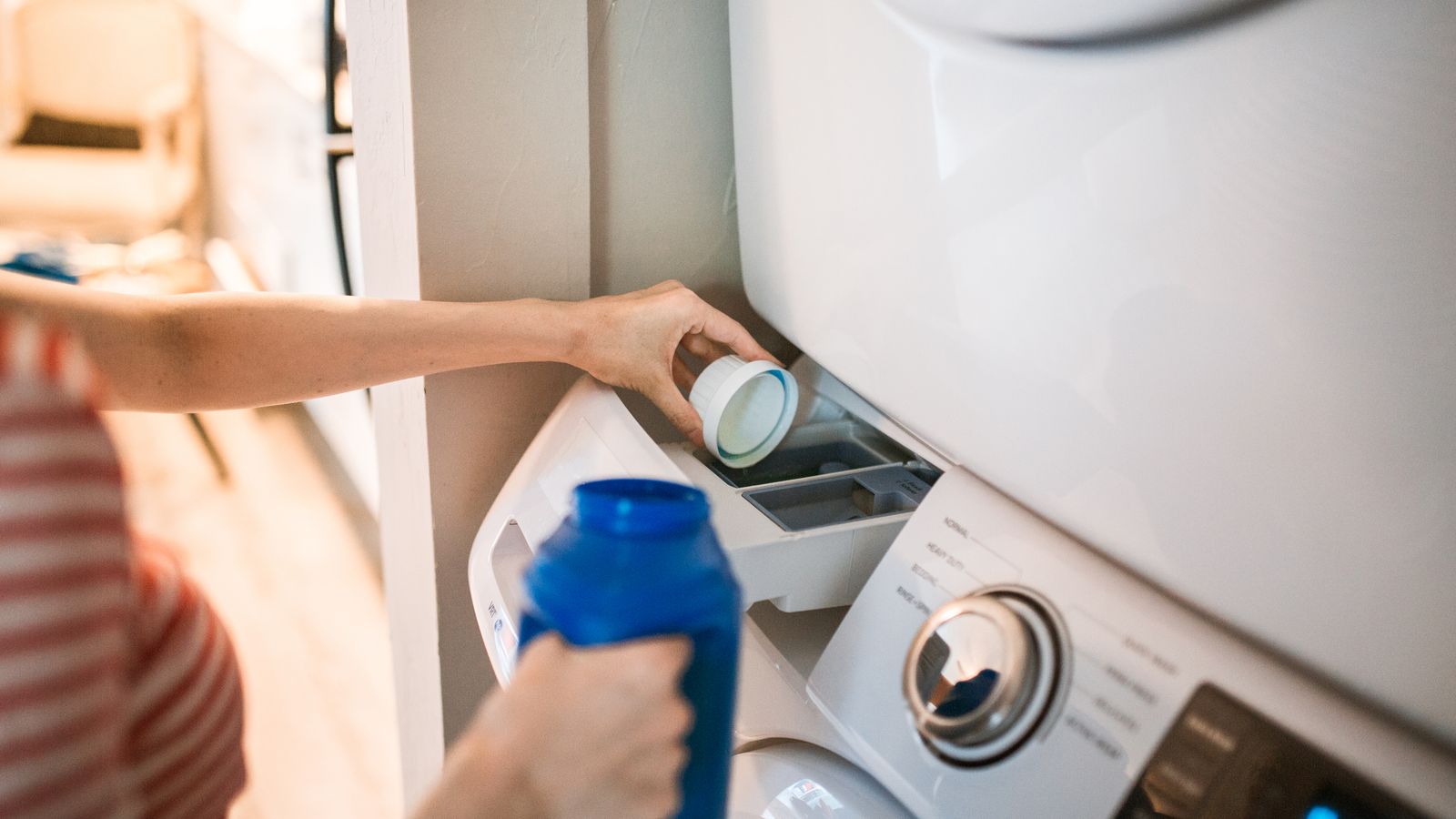 Close-up of a person pouring detergent into a front-loading washer, emphasizing household chores.