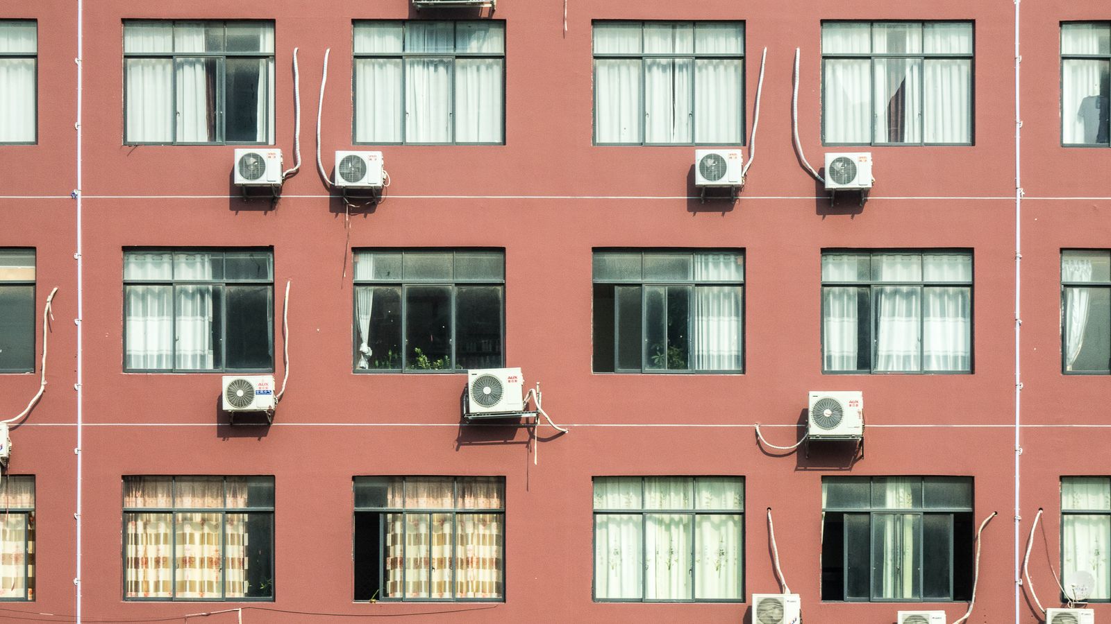 Red building exterior with multiple windows and air conditioners, showcasing urban architecture.