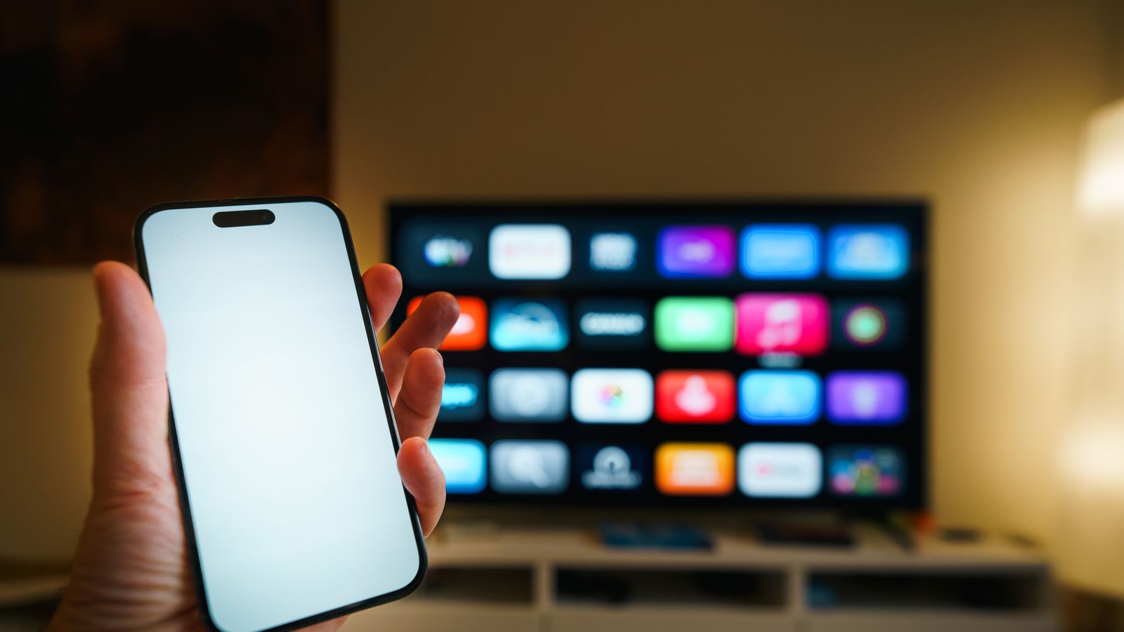 A smartphone in focus with a smart TV displaying apps in a cozy living room.