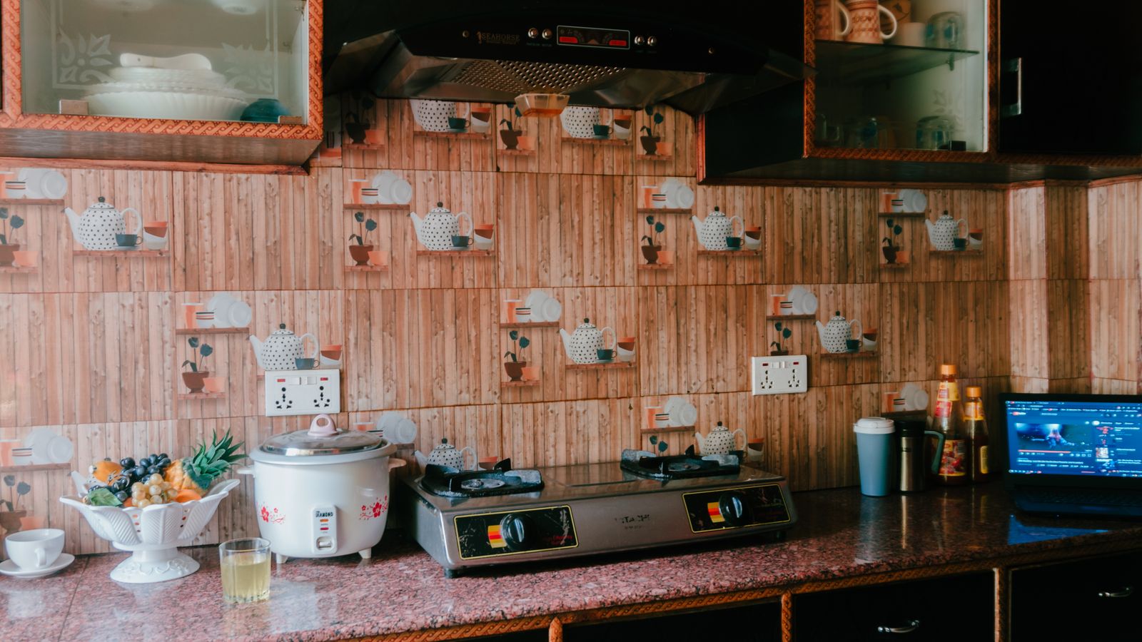 A cozy kitchen featuring a rice cooker, stove, and rustic wooden decor with glass cabinets.