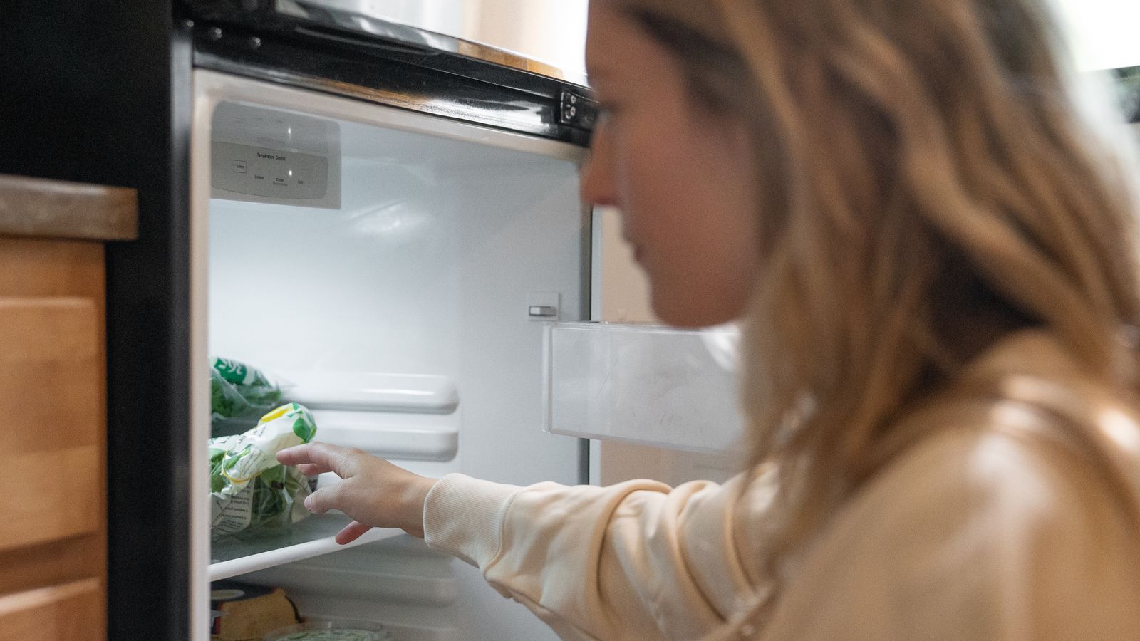 Woman grabbing vegetables from a refrigerator, symbolizing healthy living.