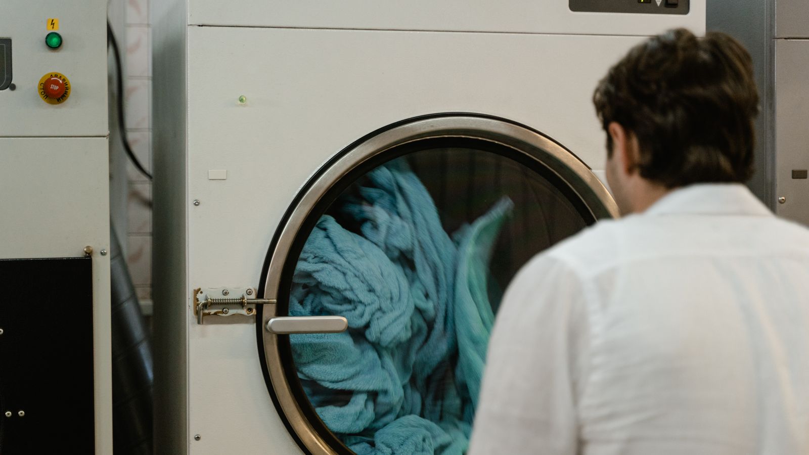 A man watches a washing machine spin in a laundromat, focusing on the process.