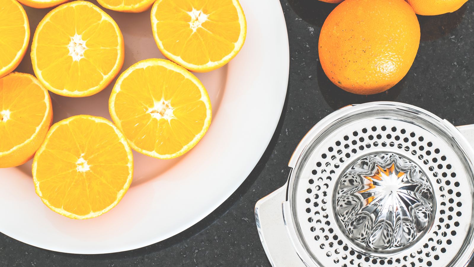 Top view of fresh oranges sliced on a white plate with a metal juicer nearby.