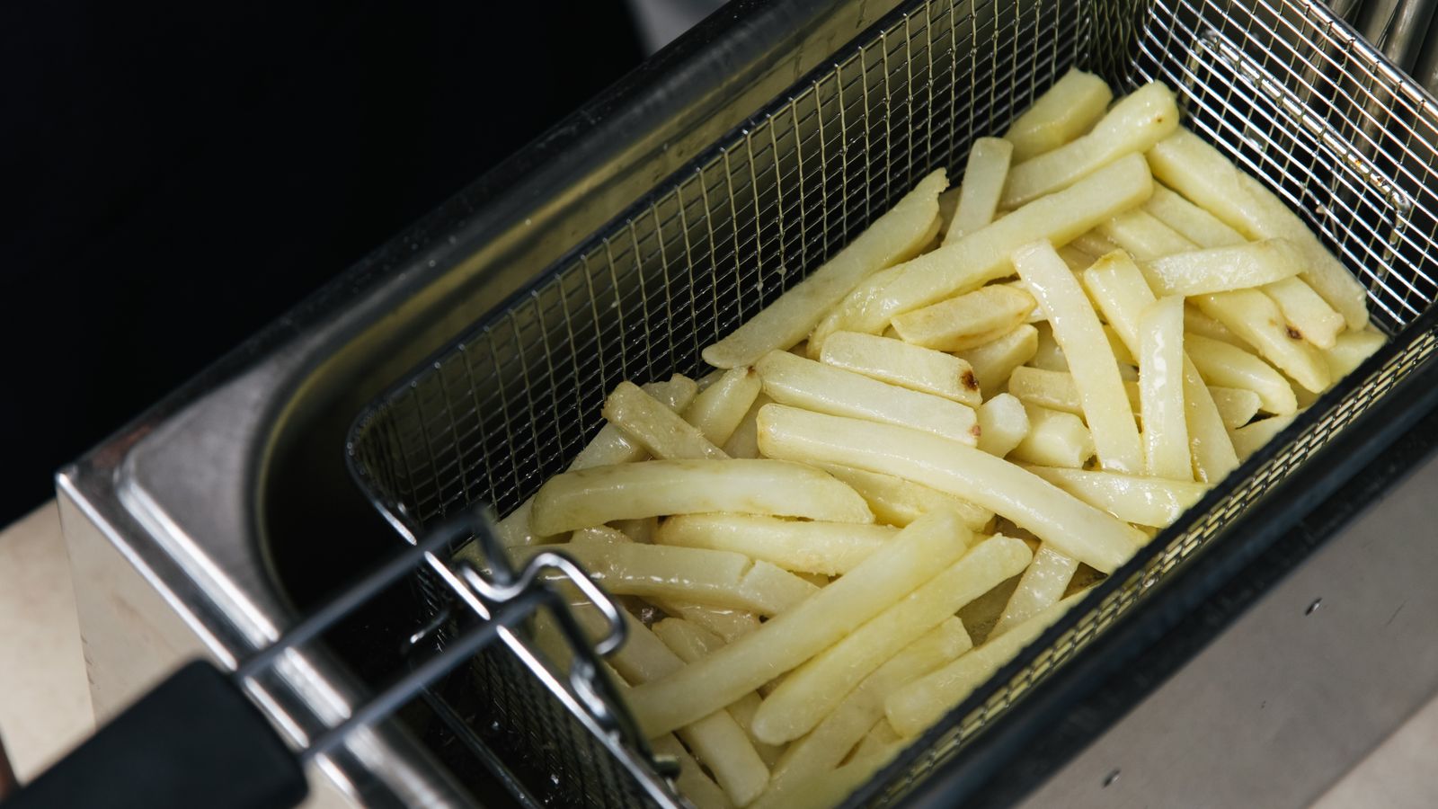 Close-up of raw french fries in a deep fryer basket ready for cooking.