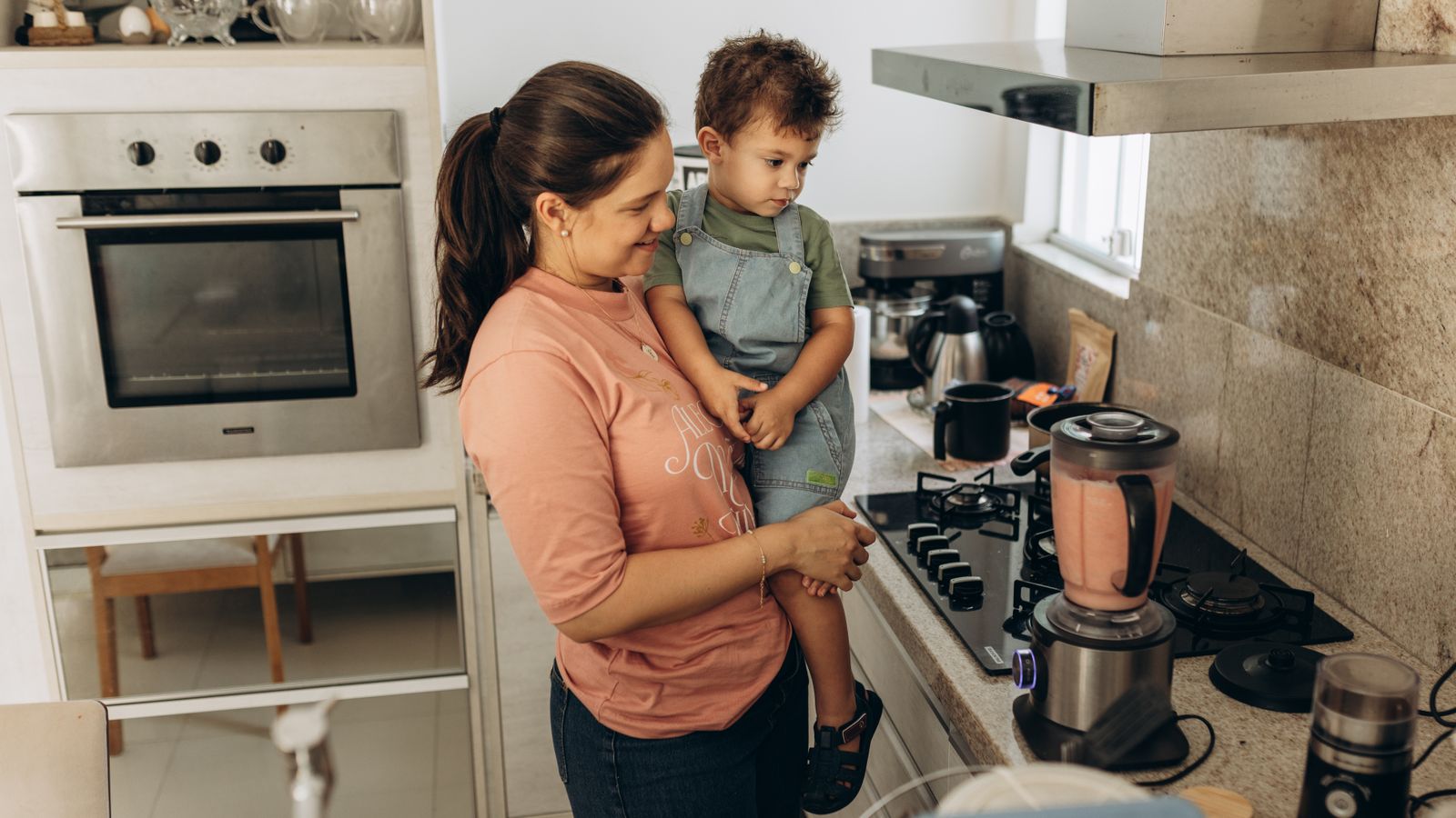 Mother and son enjoying smoothie preparation in a cozy kitchen setting.