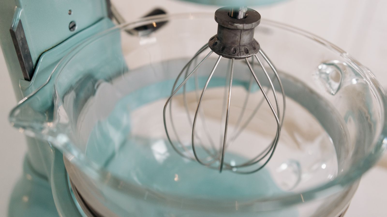 Detailed shot of a turquoise stand mixer with a whisk attachment and glass bowl, ideal for baking.