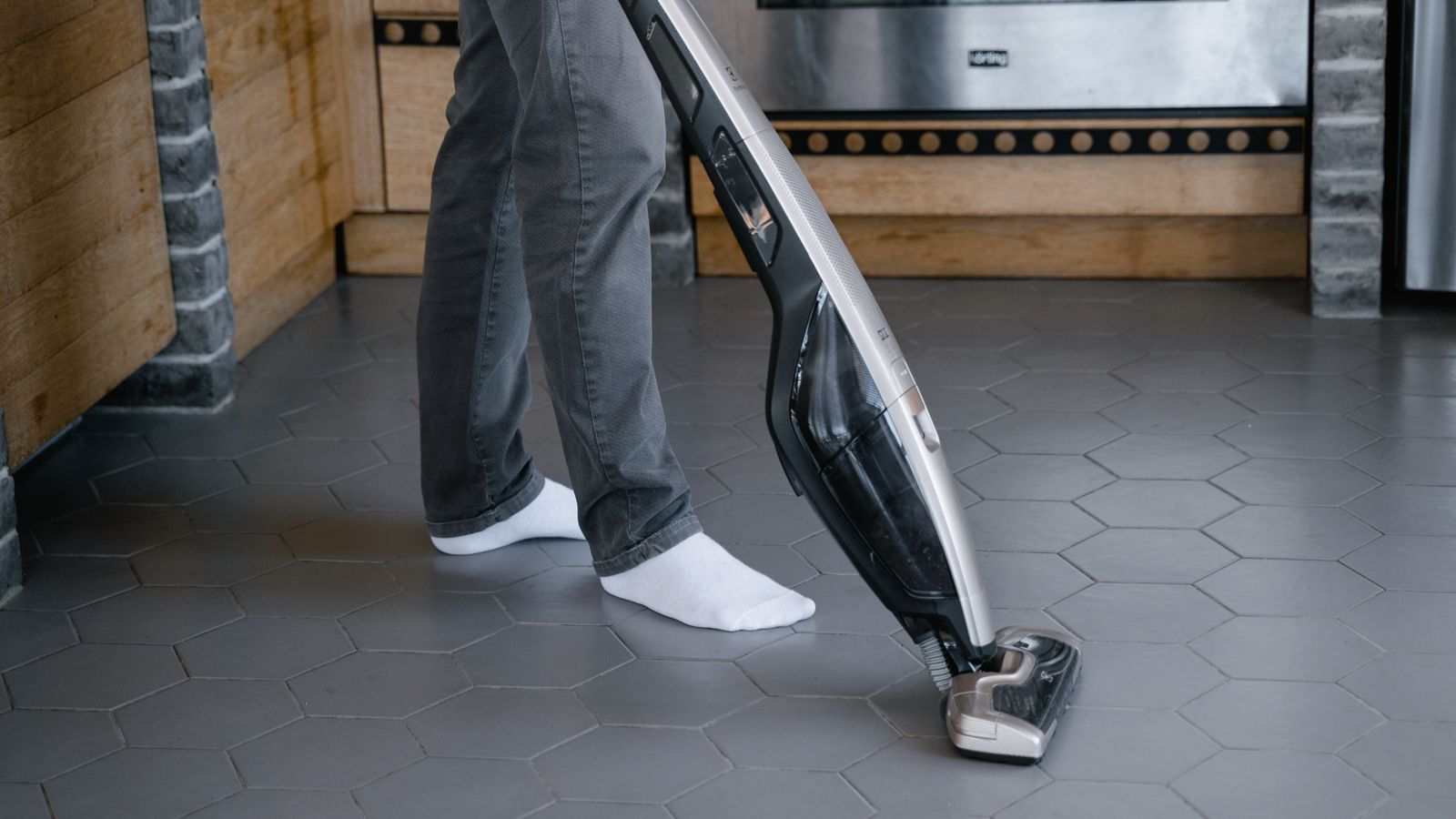 A person cleaning a tiled floor with a modern vacuum cleaner indoors.