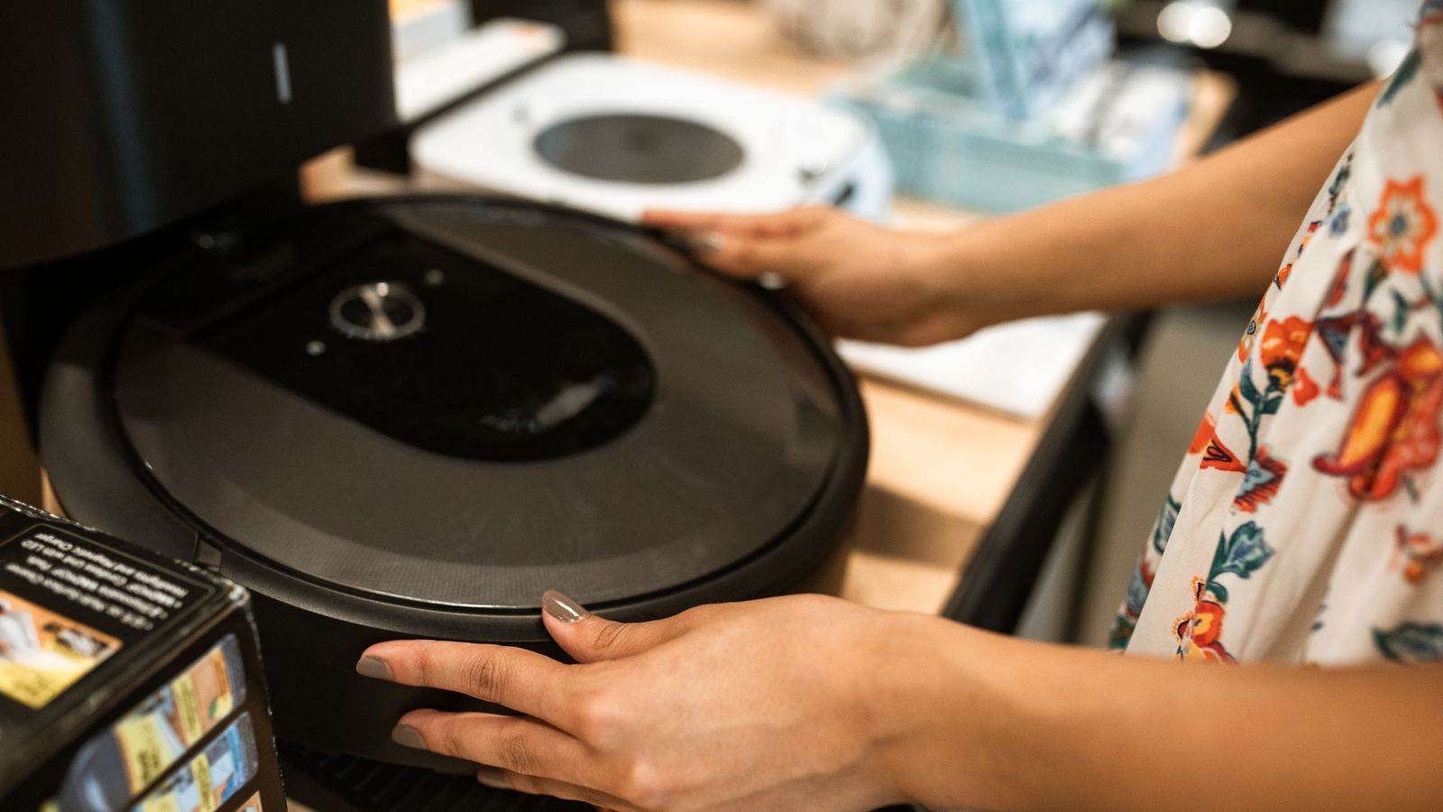 A customer examines a sleek robotic vacuum cleaner in a modern store.