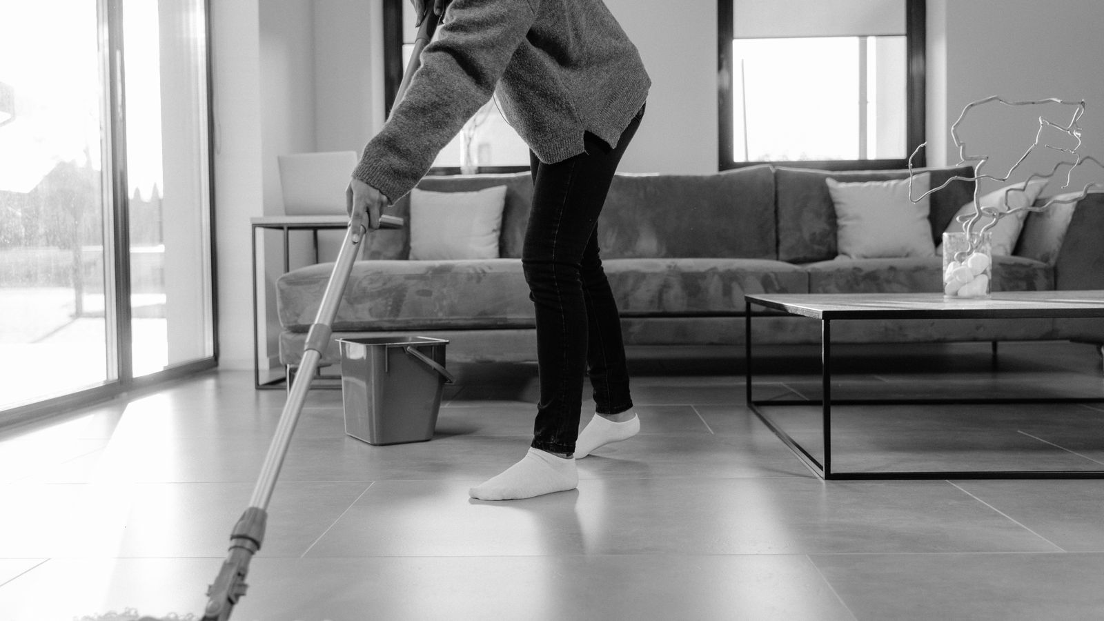 A grayscale photo of a person mopping the floor in a modern living room.
