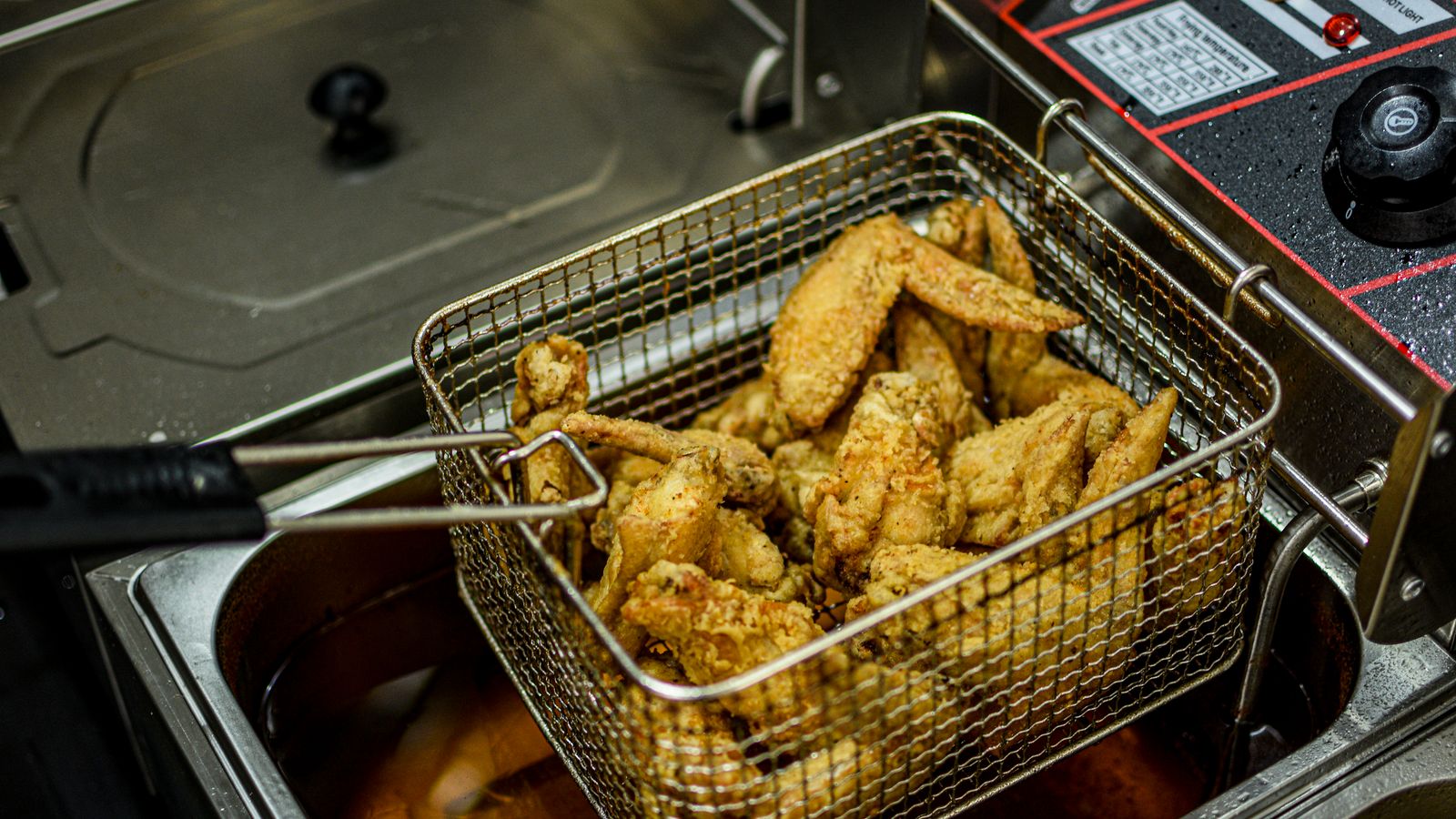 Golden brown chicken wings freshly fried in a commercial deep fryer.