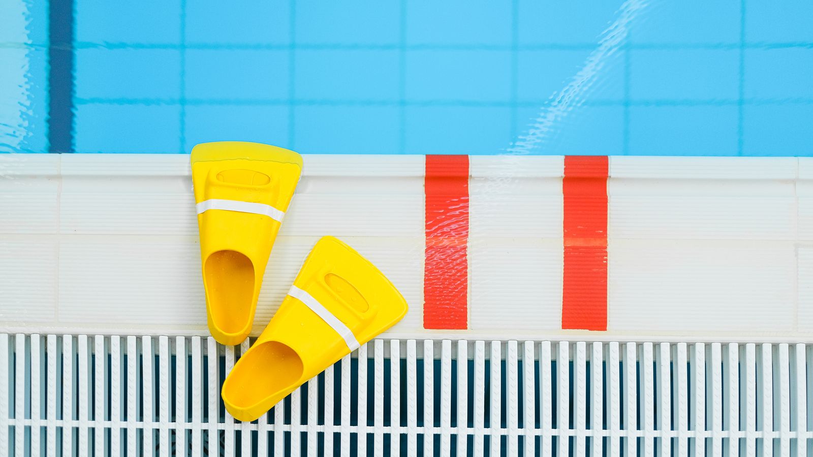 Vibrant yellow swim fins placed by the edge of a clear swimming pool, ideal for aquatic sports.