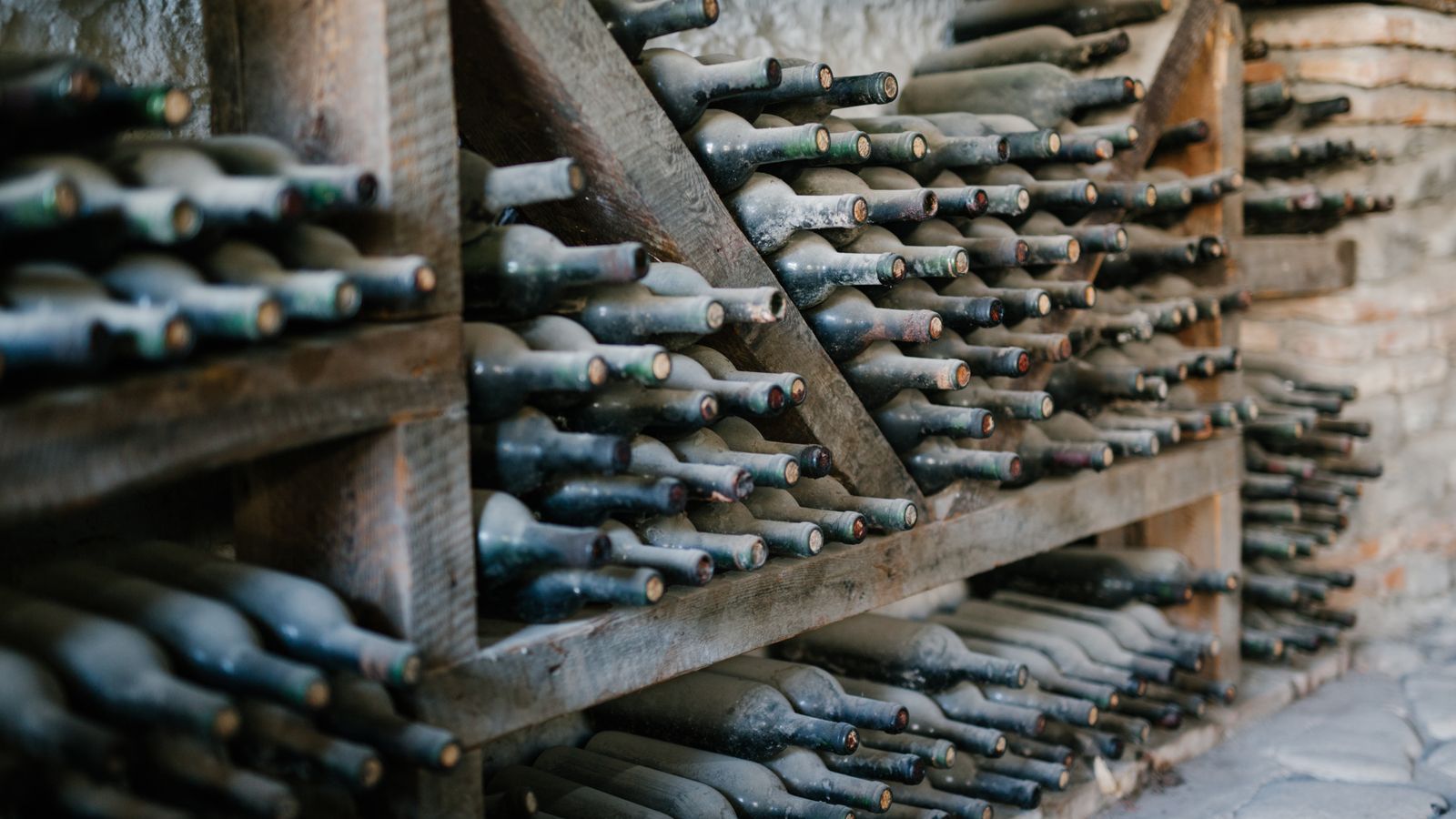 Dusty alcoholic beverage bottles with coiled corks on wooden shelves at wine farm