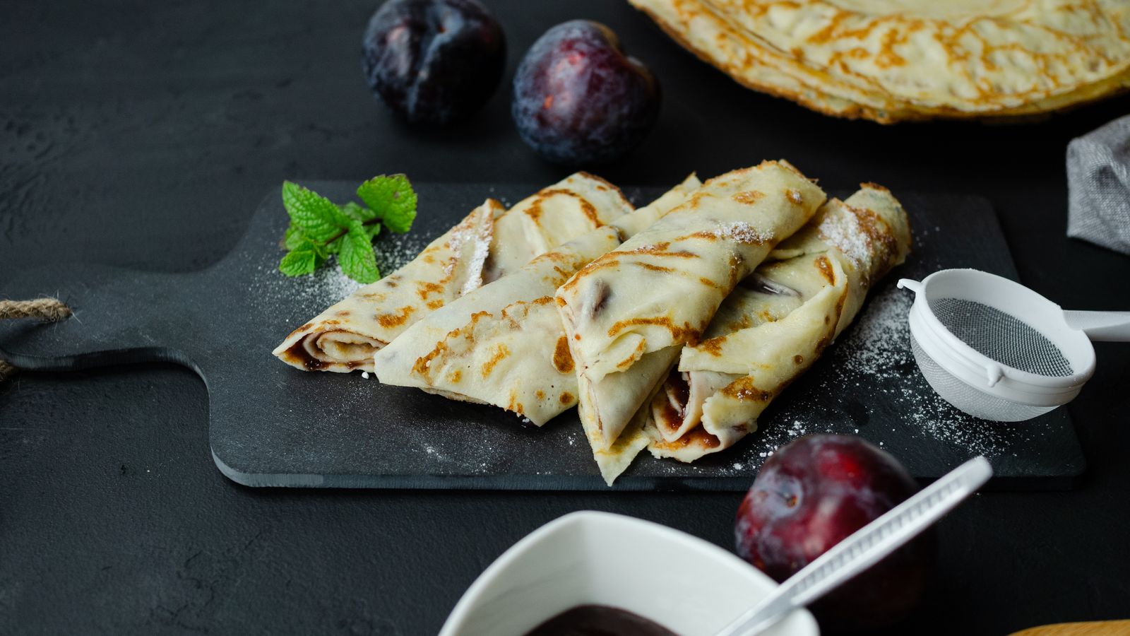 Delicious homemade crepes filled with jam and fresh plums on a serving board.
