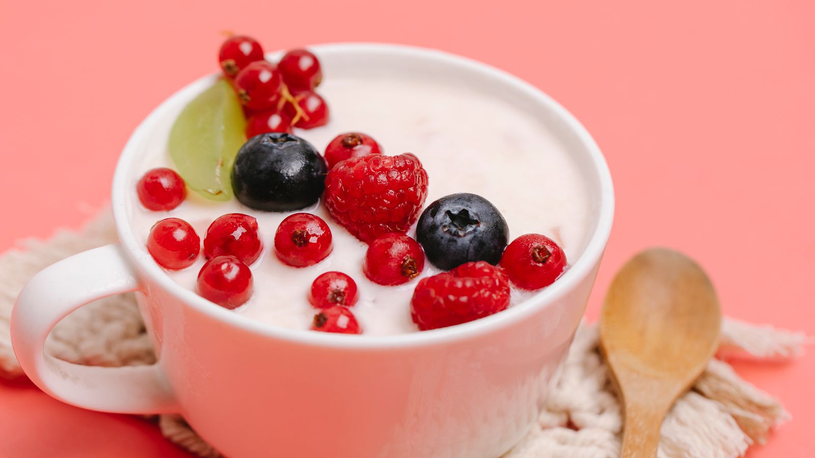From above of delicious homemade yogurt in white ceramic mug decorated with assorted berries and served on pink table with wooden spoon