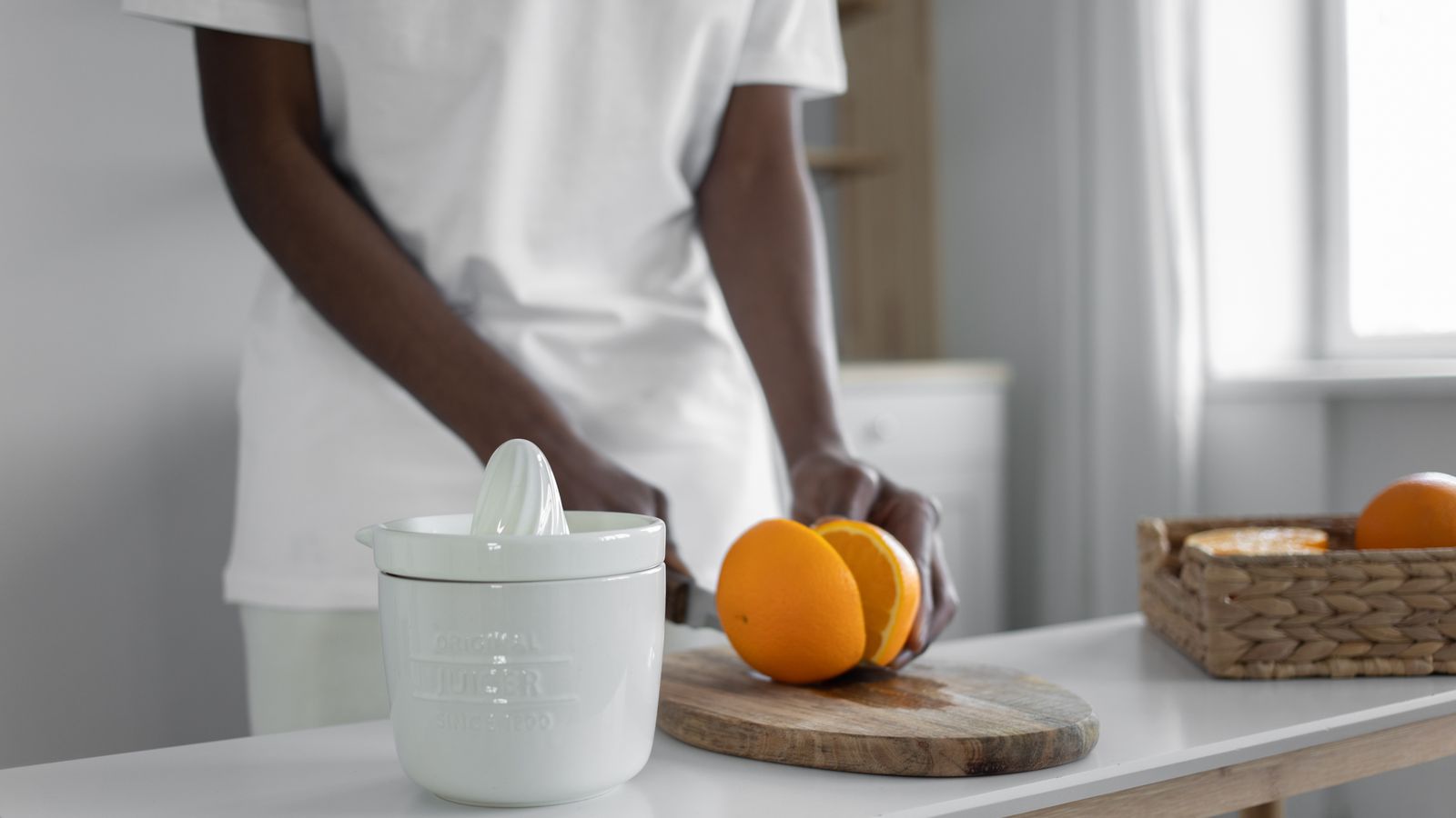 A person slicing oranges on a cutting board next to a white juicer in a bright kitchen.